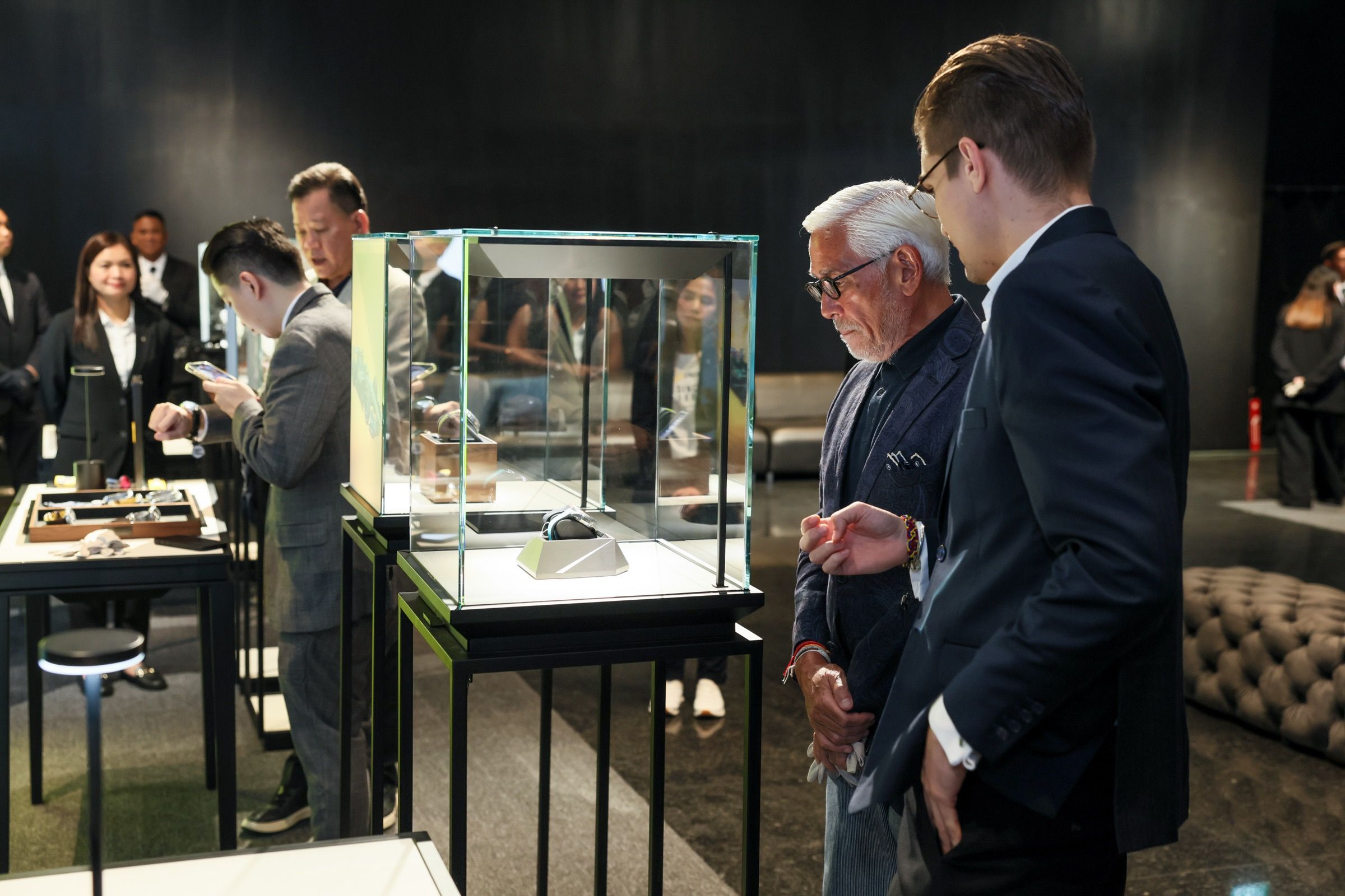 A senior visitor and representative intently viewing a luxury watch inside a glass display case at Lucerne Watch Week