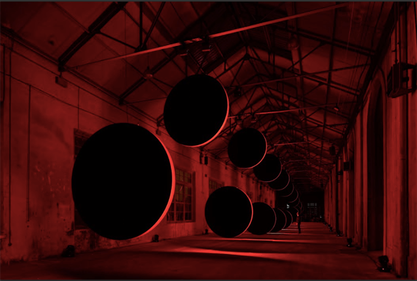 Large black eclipse discs line a red-lit industrial corridor in SpY’s “Eclypses” in Oviedo, Spain