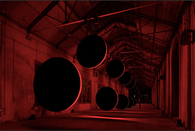 Large black eclipse discs line a red-lit industrial corridor in SpY’s “Eclypses” in Oviedo, Spain