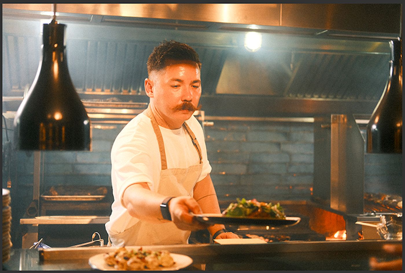 Chef Josh Boutwood plates a dish of greens at the pass of his fiery open-grill kitchen