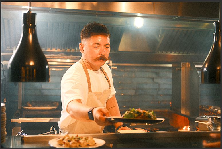 Chef Josh Boutwood plates a dish of greens at the pass of his fiery open-grill kitchen