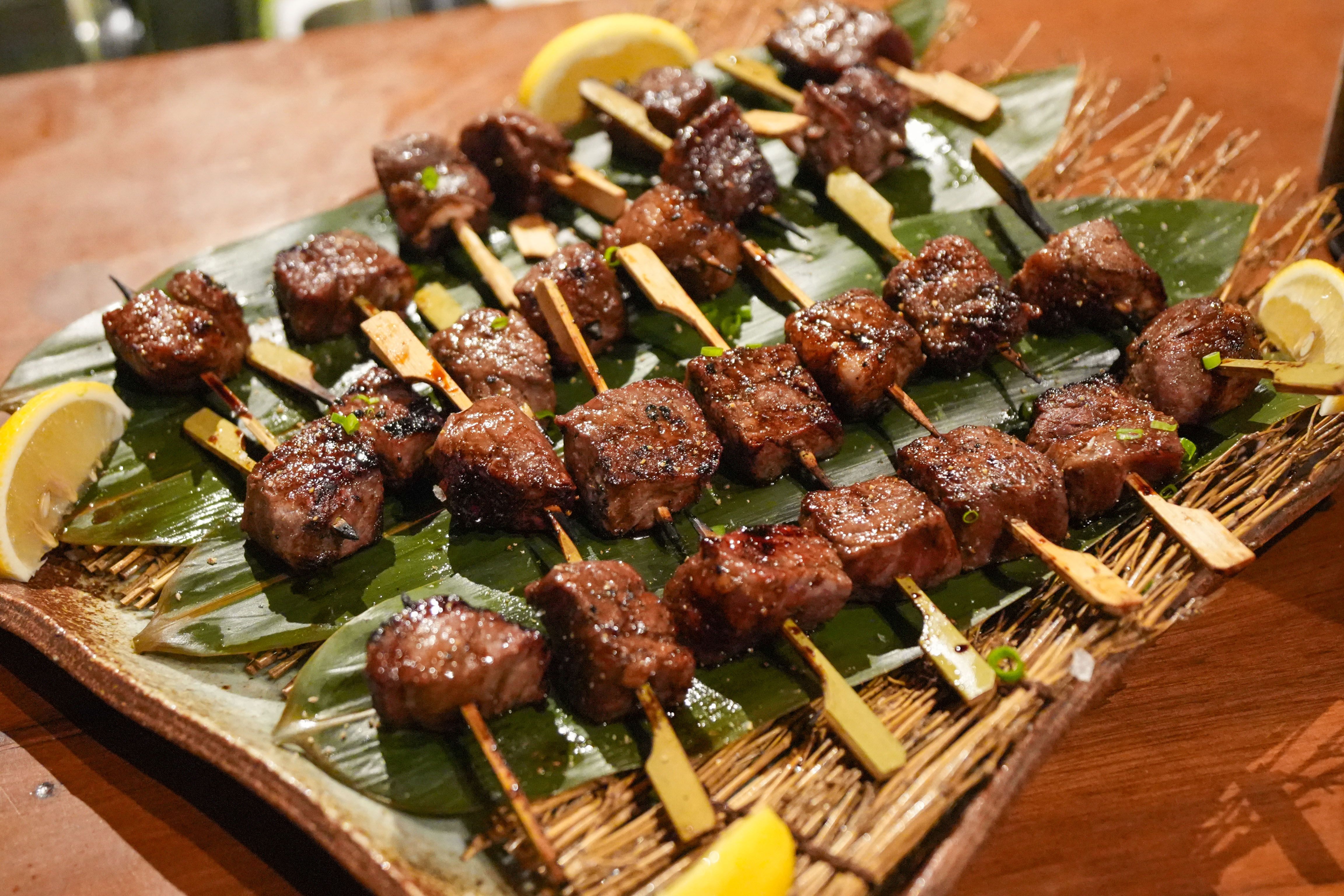 Grilled Japanese wagyu beef skewers arranged on banana leaves with lemon wedges on a wooden board