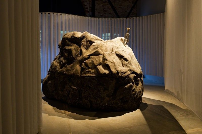 Mark Salvatus installation of a large boulder with a trumpet emerging from its top, ringed by white curtains at the Philippine Pavilion in Venice