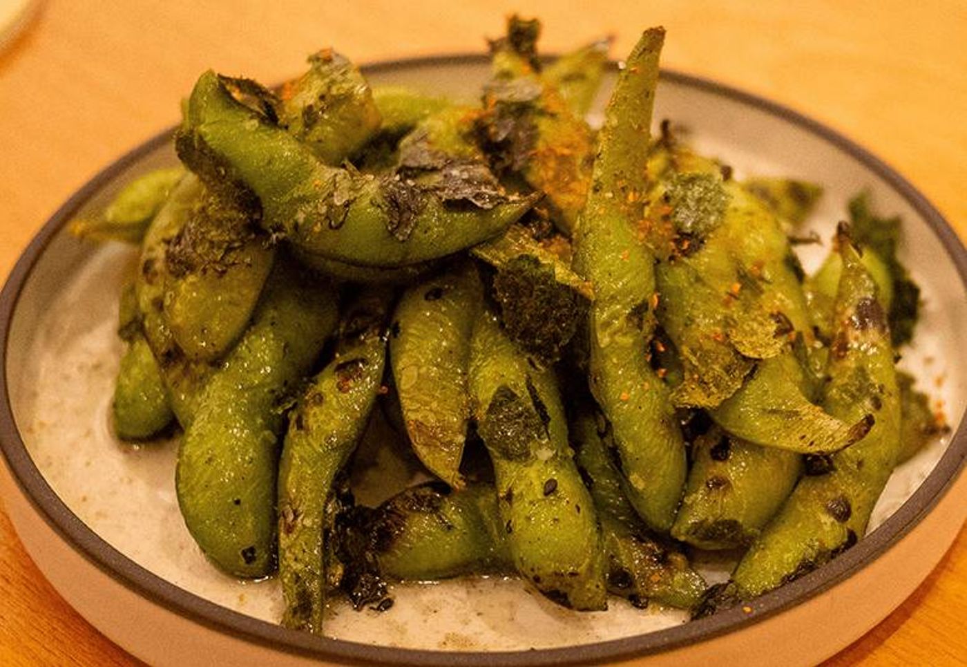 Pile of charred edamame pods flecked with seasoning on a bed of coarse salt in a white bowl