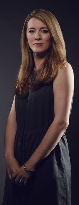 Annabel Jones in a sleeveless charcoal dress, hands clasped, against a dark studio backdrop