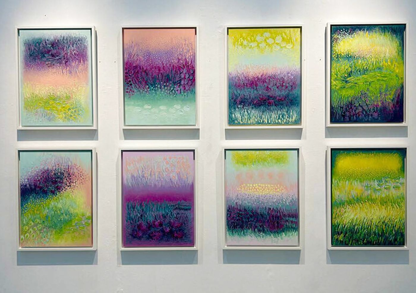 Eight small framed abstract paintings arranged in two rows of four on a white wall, each filled with layered brushwork in greens, purples, pinks and yellows