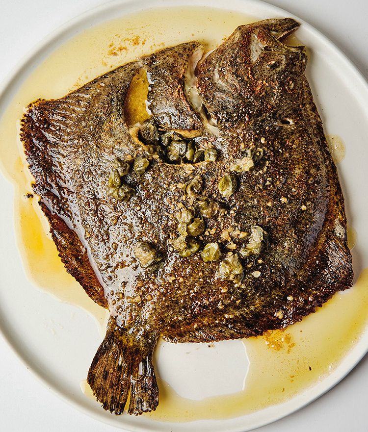 Whole grilled turbot on a white plate, glossed with brown butter and scattered with capers