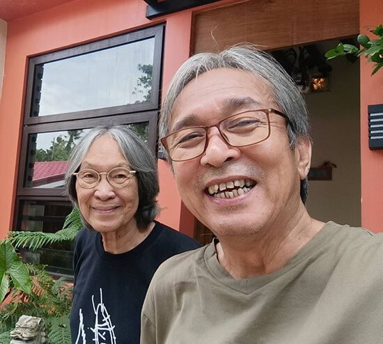 Selfie of a smiling man in glasses with a gray-haired companion outside an orange building