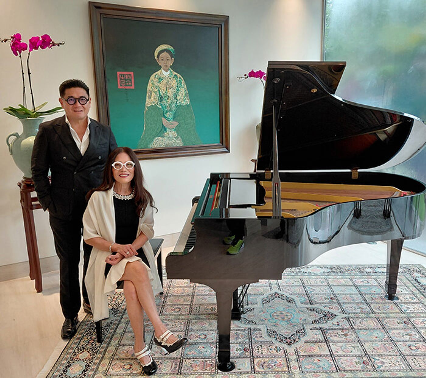 Anton T. Huang stands beside Cecile Licad, seated at a grand piano near a green portrait painting