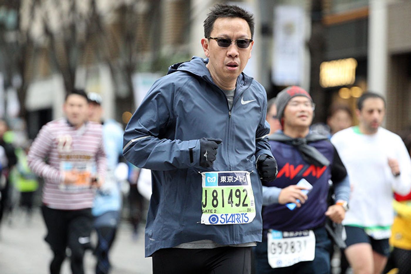 Emerson Yao running among other competitors in a grey jacket and sunglasses, a Tokyo Metro race bib on his chest