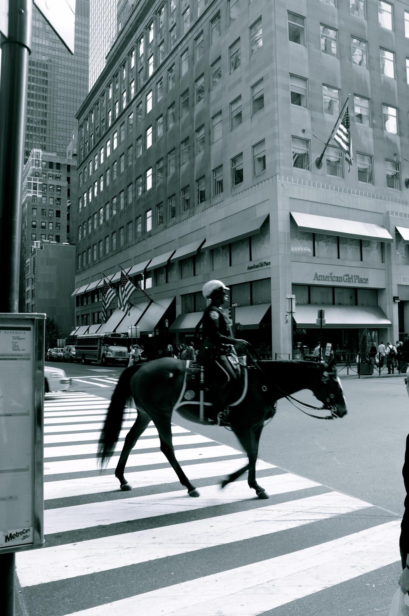 Mounted police officer crossing a Manhattan street past the American Girl Place storefront