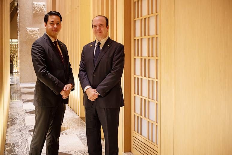 Yoki Takeuchi and Jan William Marshall in dark suits in a wood-latticed corridor of Hotel Okura Manila