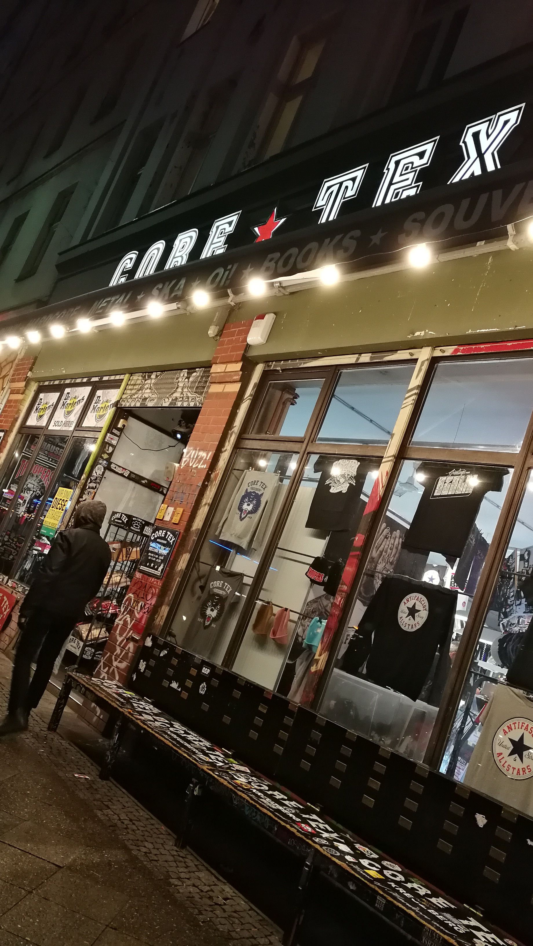 String lights glowing over the Core Tex punk shop storefront and its sticker-covered bench at night