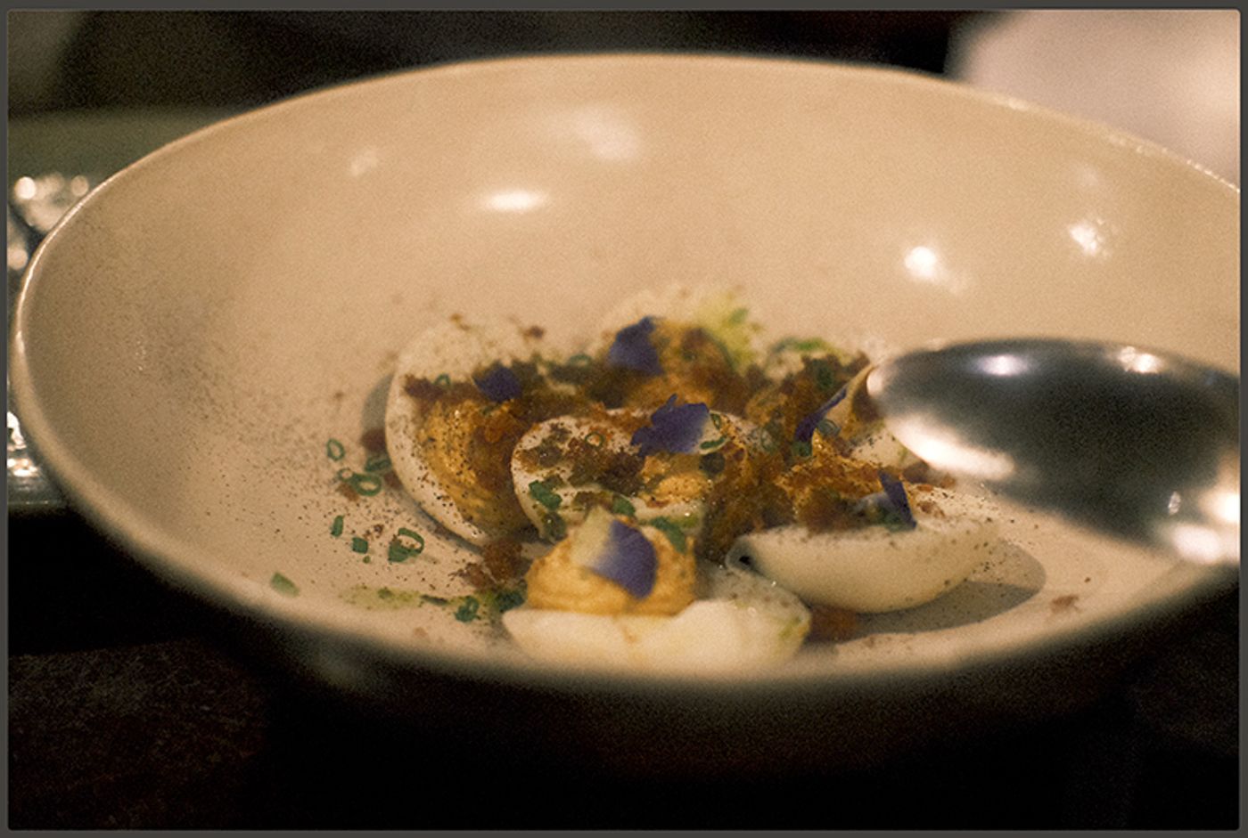 Chef Josh Boutwood’s deviled eggs dusted with spice and scattered with chives and violet petals in a speckled ceramic bowl
