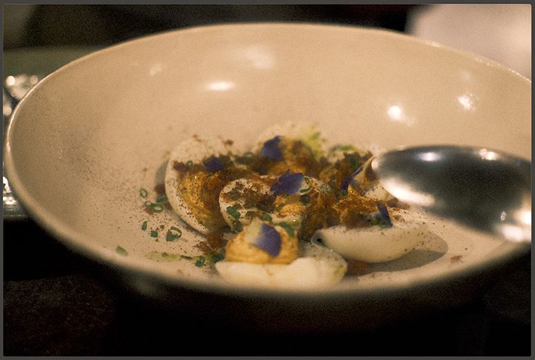 Chef Josh Boutwood’s deviled eggs dusted with spice and scattered with chives and violet petals in a speckled ceramic bowl