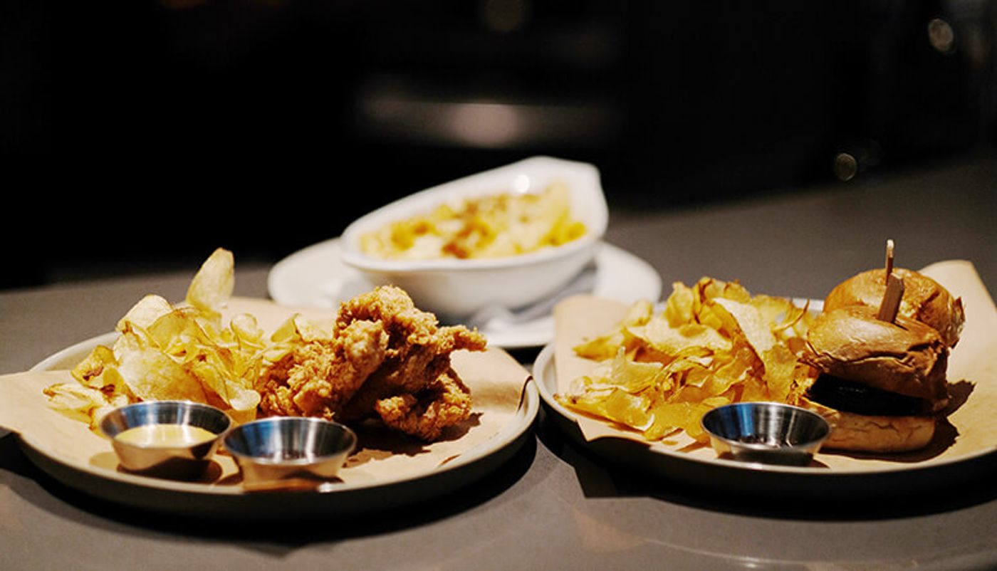Chicken fingers, a slider and mac and cheese with crisps and dipping sauces on a dark tabletop