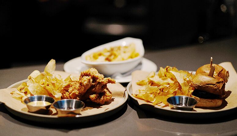 Chicken fingers, a slider and mac and cheese with crisps and dipping sauces on a dark tabletop