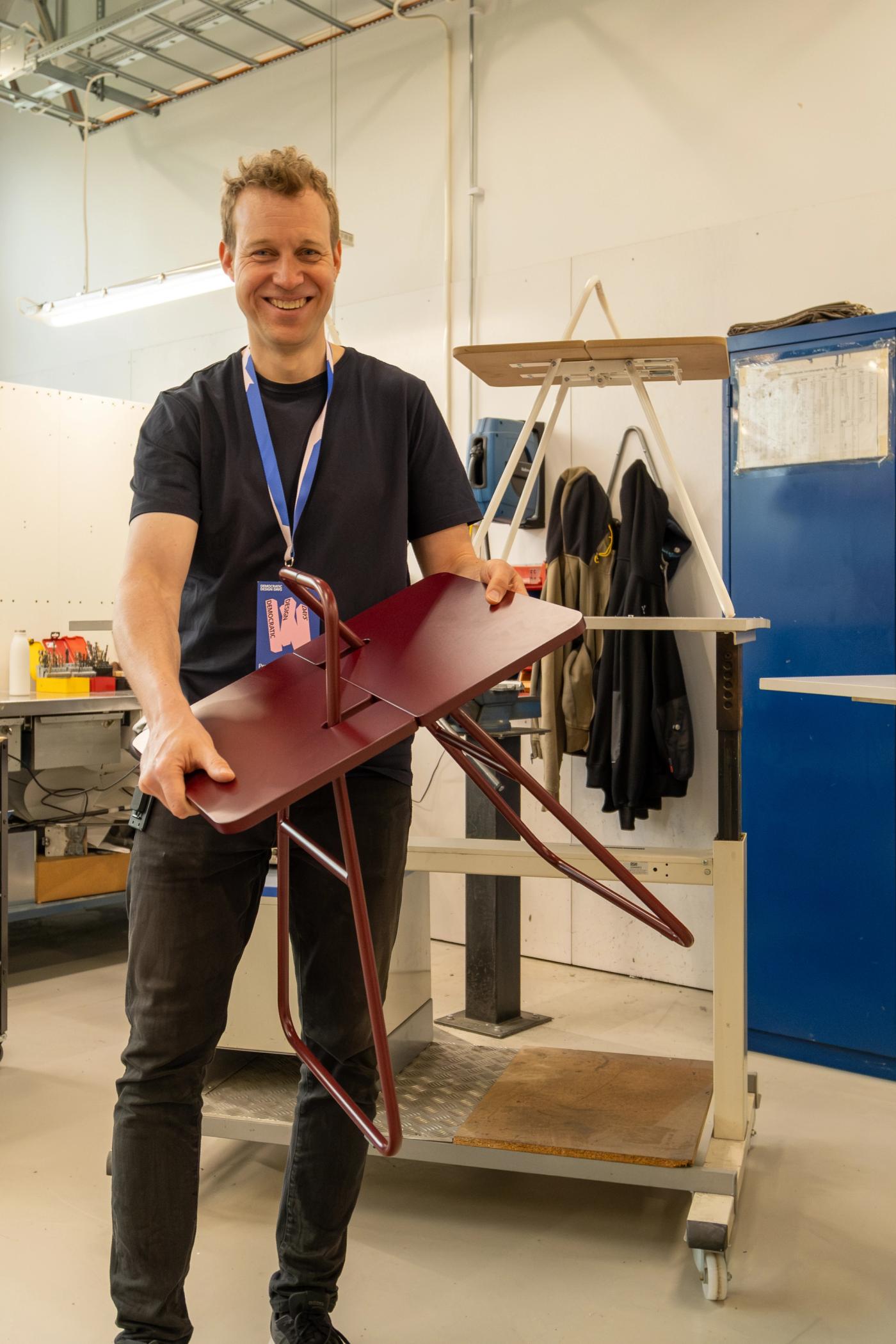 Designer David Wahl carrying his folded dark red portable table through an IKEA prototype workshop