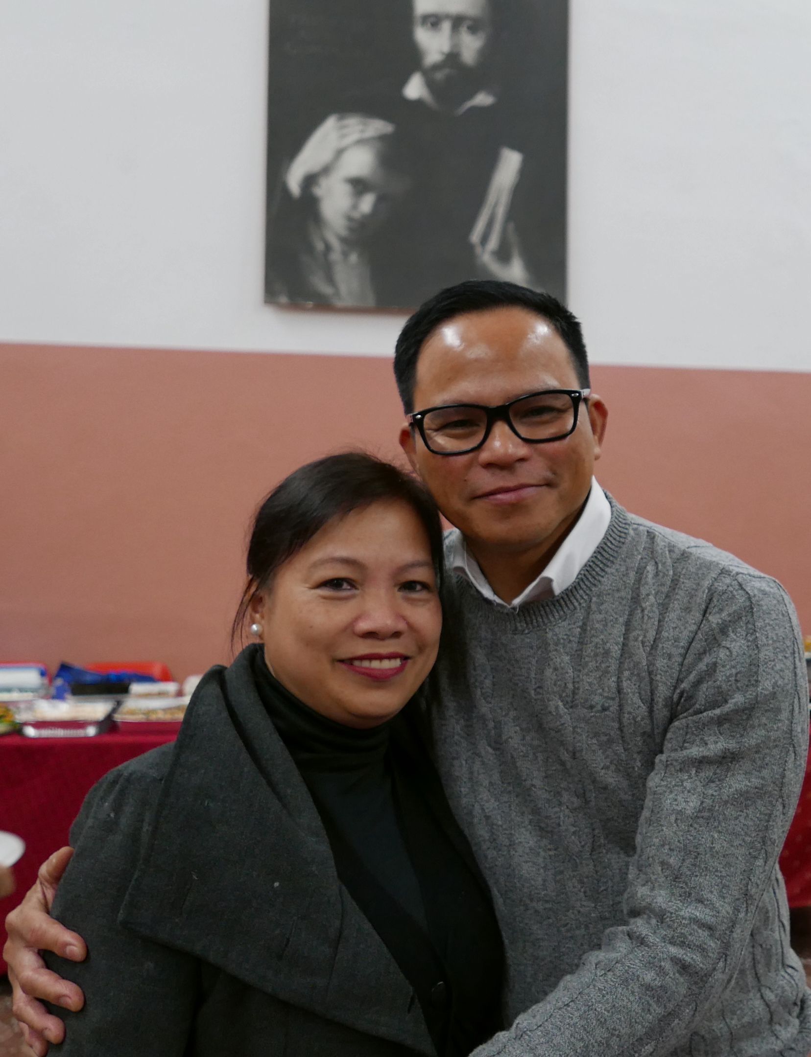 Nonon and Thess Malinay sit together on a wooden bench, in a green jacket and a brown shearling jacket