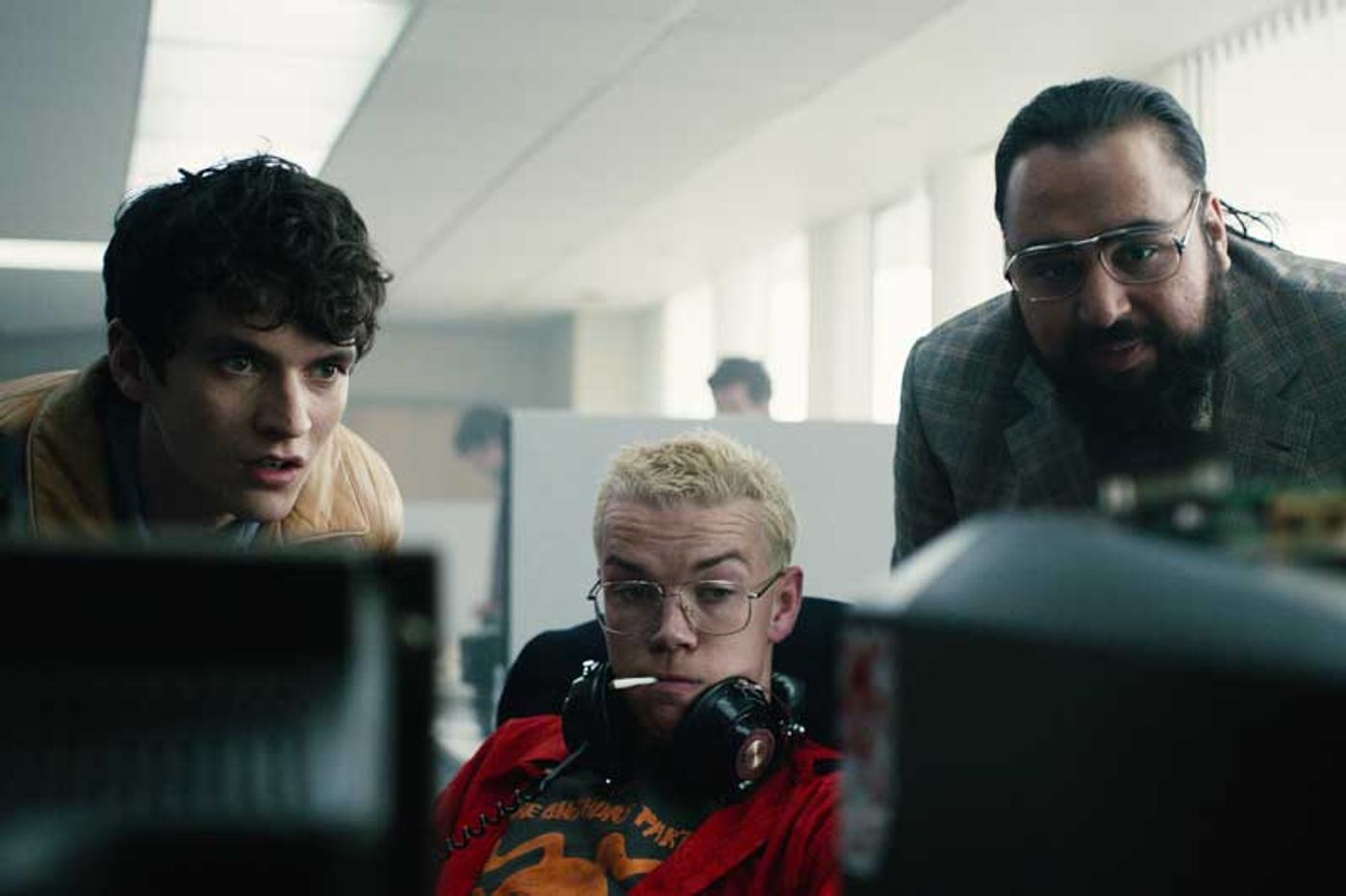 Fionn Whitehead, Will Poulter and Asim Chaudhry huddle around a computer monitor in a Bandersnatch scene