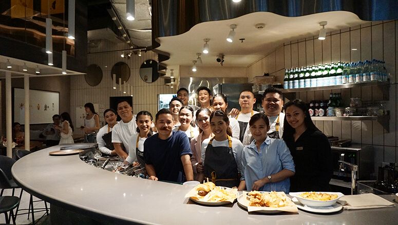 Ember’s kitchen and service team gathered behind a curved counter in the white-tiled open kitchen