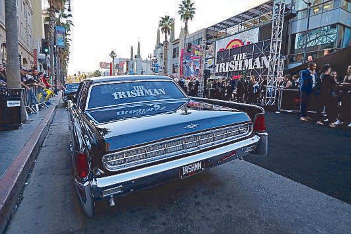 A black vintage Lincoln wrapped in The Irishman signage parked amid crowds on Hollywood Boulevard