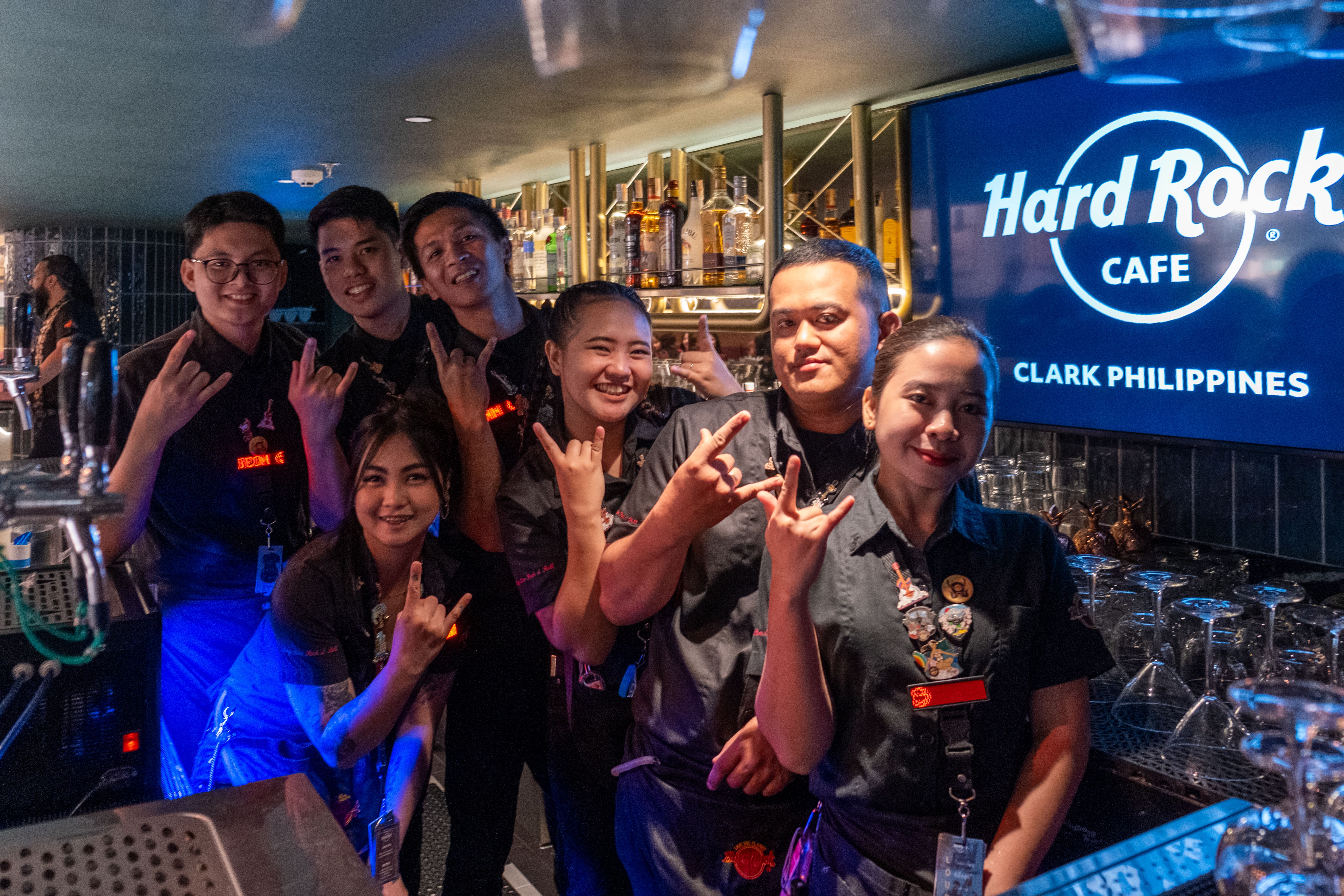Seven bar staff in black flash devil-horn signs beneath the Hard Rock Cafe Clark Philippines sign
