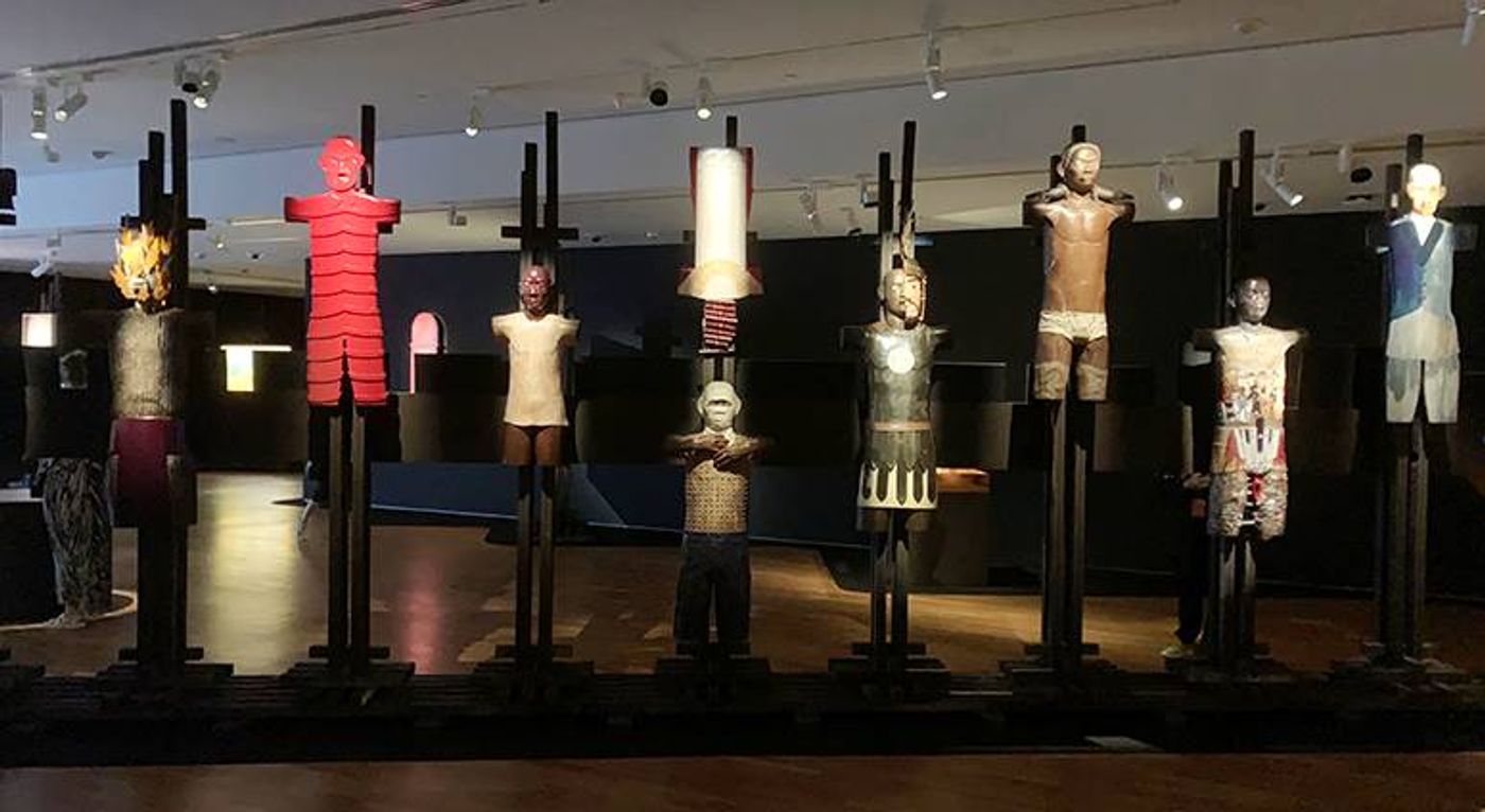 Robert Feleo’s Ang Retablo ng Bantaoay: carved standing figures mounted on dark posts in a dim gallery