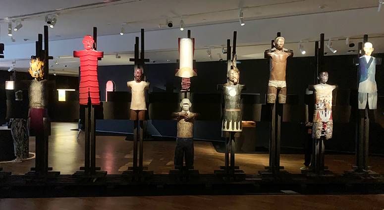 Robert Feleo’s Ang Retablo ng Bantaoay: carved standing figures mounted on dark posts in a dim gallery