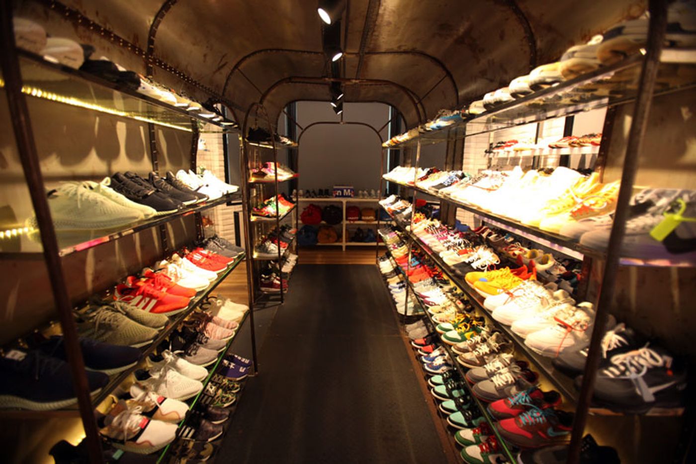 A narrow room with sneakers on lit glass shelves running down both walls to the far end