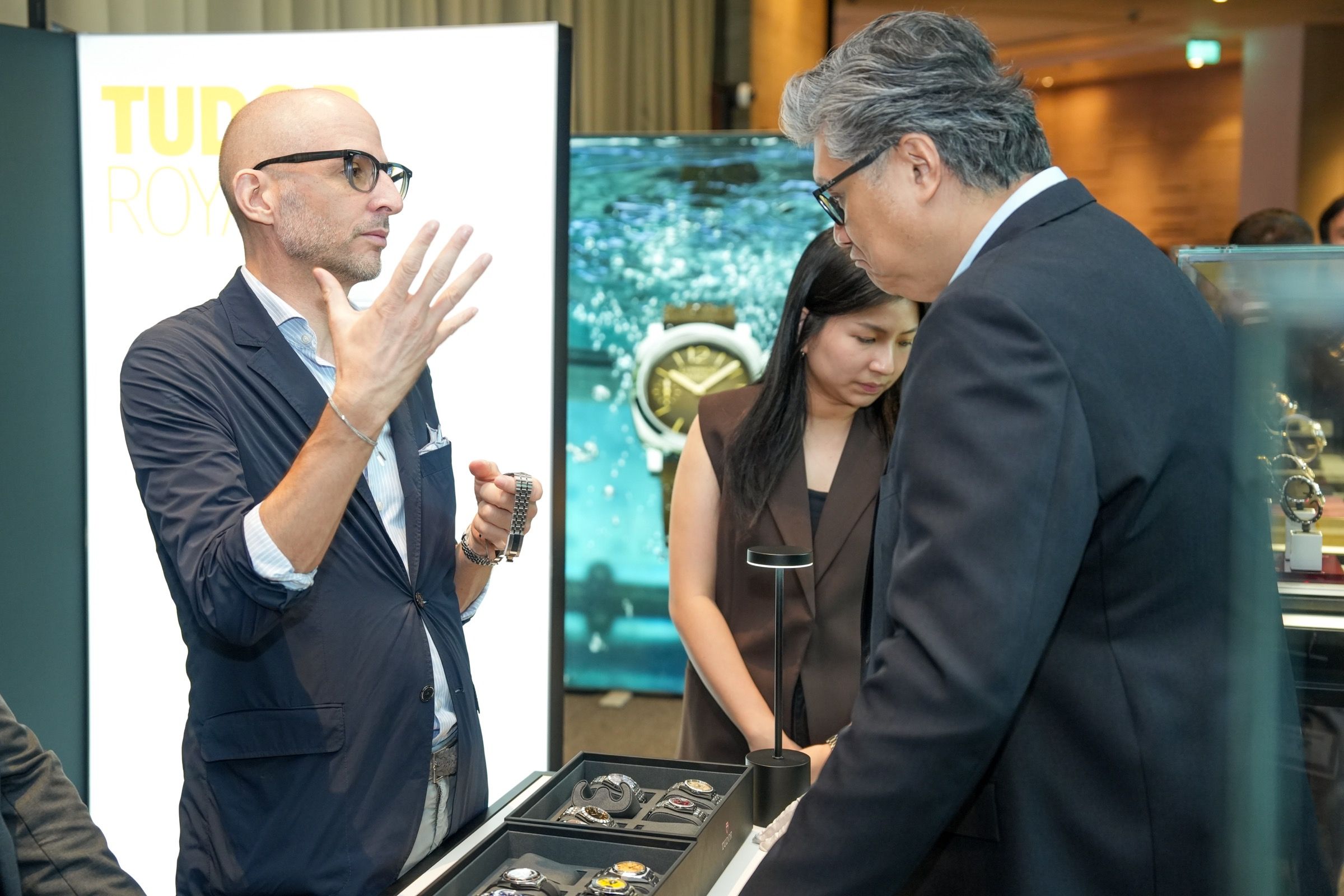 A brand representative gesturing while presenting Tudor watches in display trays to guests at Lucerne Watch Week