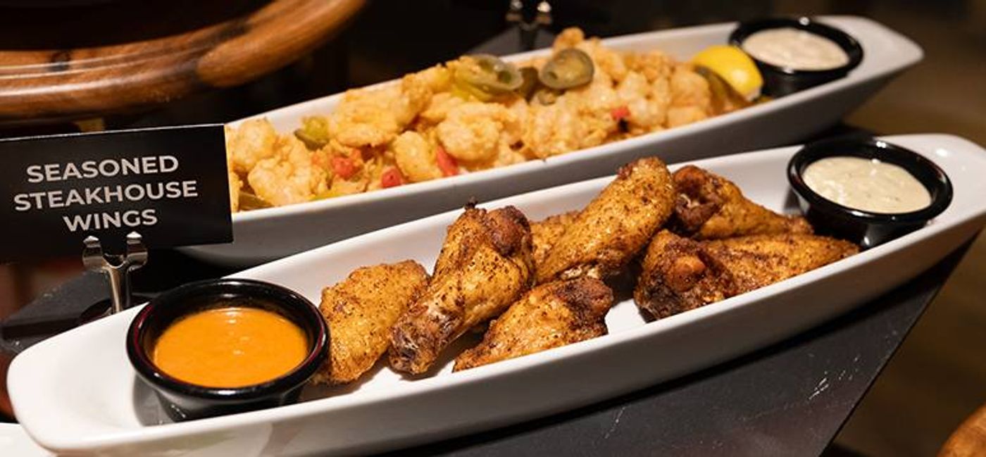 Seasoned steakhouse wings with orange dipping sauce, a platter of fried appetizers behind