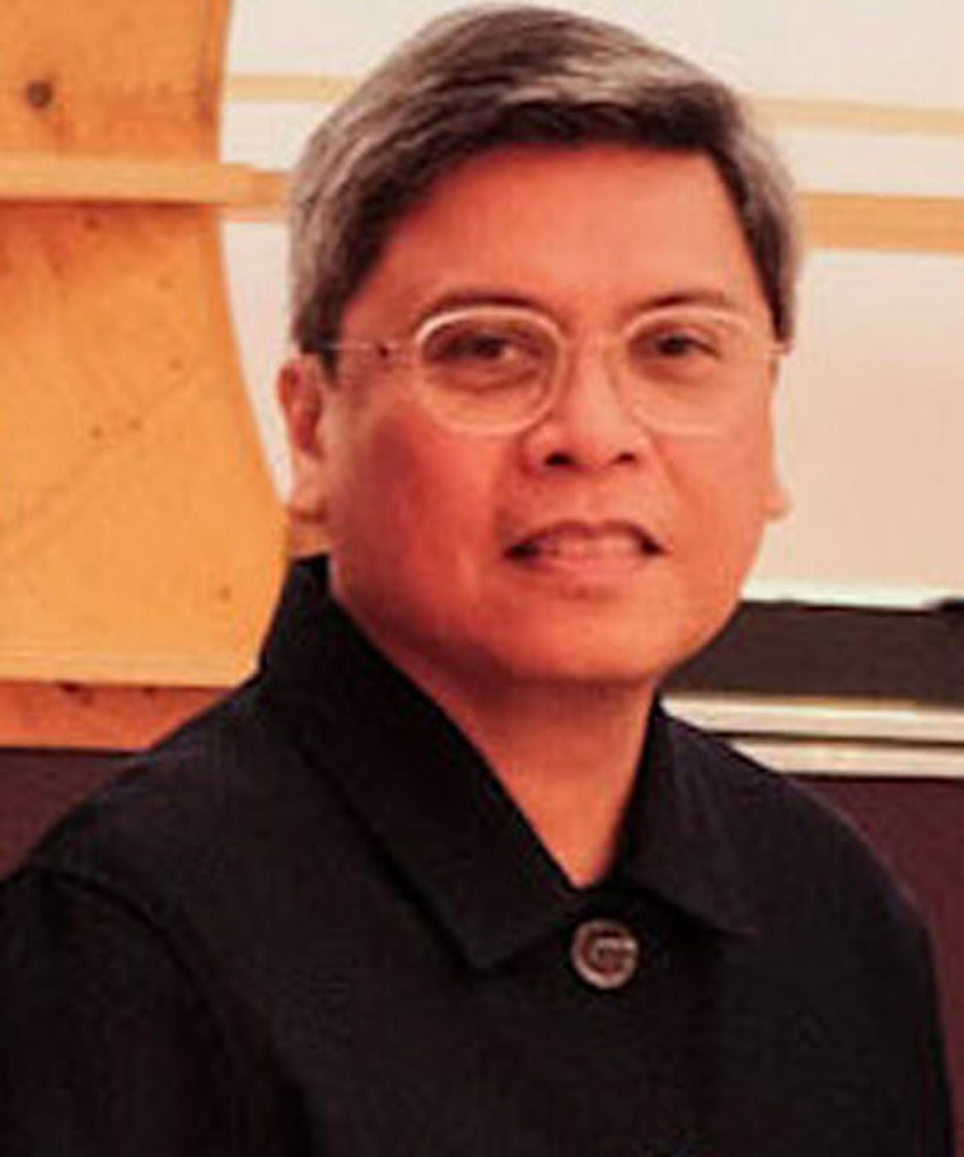 Dr. Patrick Flores in a dark jacket and wire-rimmed glasses, smiling before a pale wooden panel of the stand