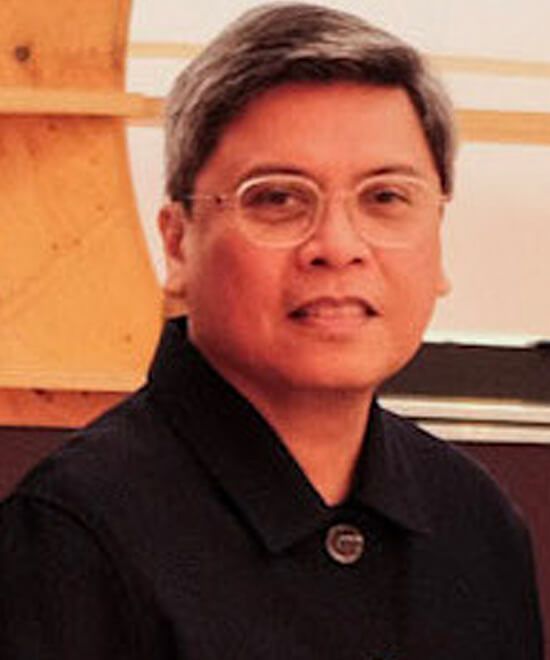 Dr. Patrick Flores in a dark jacket and wire-rimmed glasses, smiling before a pale wooden panel of the stand
