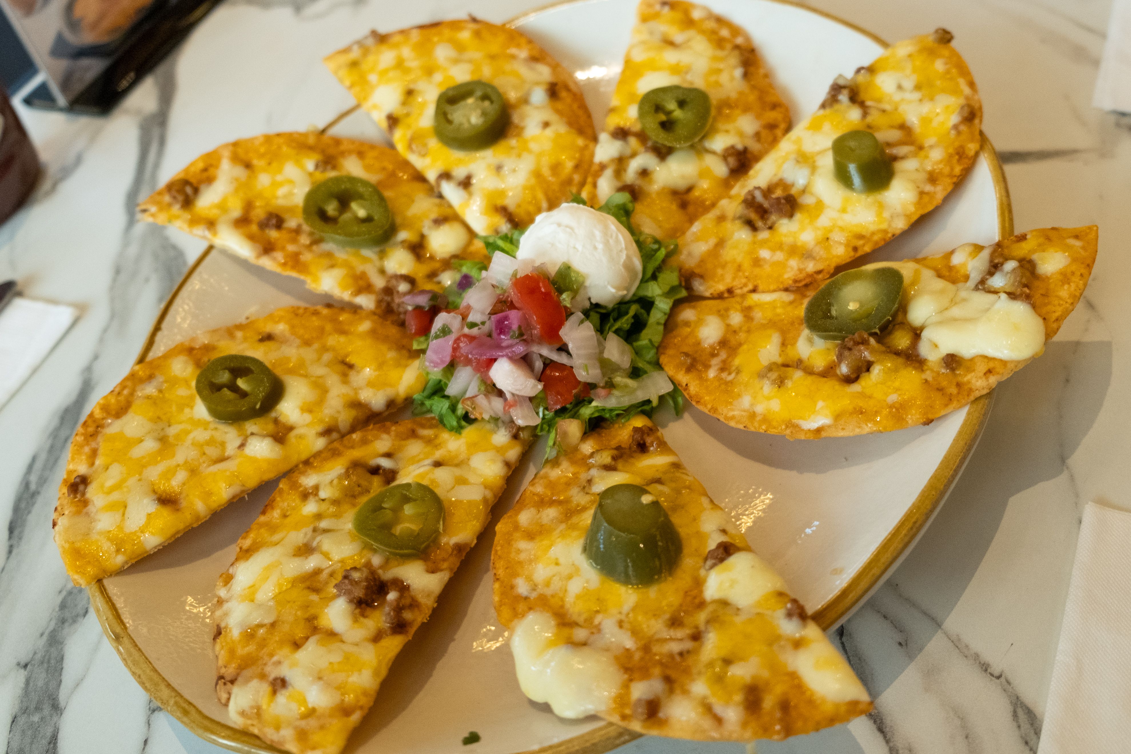 Cheese-topped tostado wedges dotted with jalapeno slices arranged around salsa and sour cream