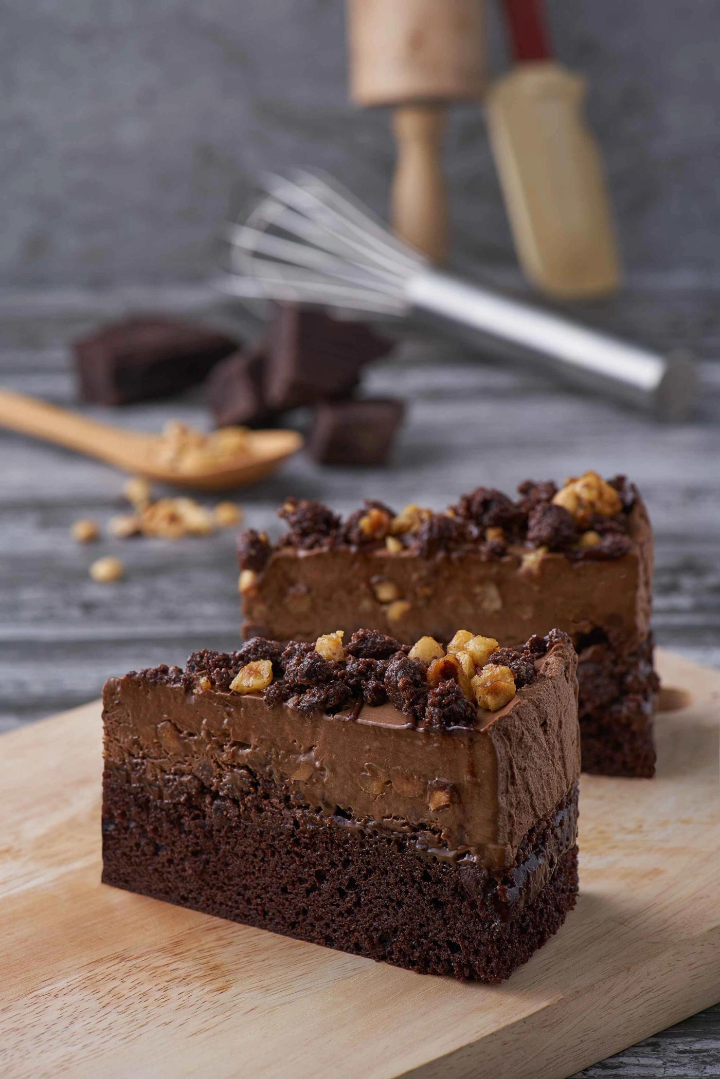 Two slices of Secret Recipe’s Chocolate Odyssey, layered chocolate mousse and sponge topped with walnuts and chocolate crumble, on a wooden board