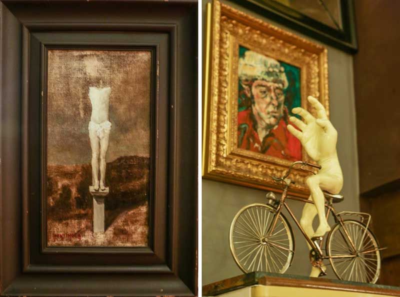 Left, a small dark painting of a lone figure on a pillar; right, a gilt-framed portrait of an older man beside a pale sculpture of a nude riding a bicycle