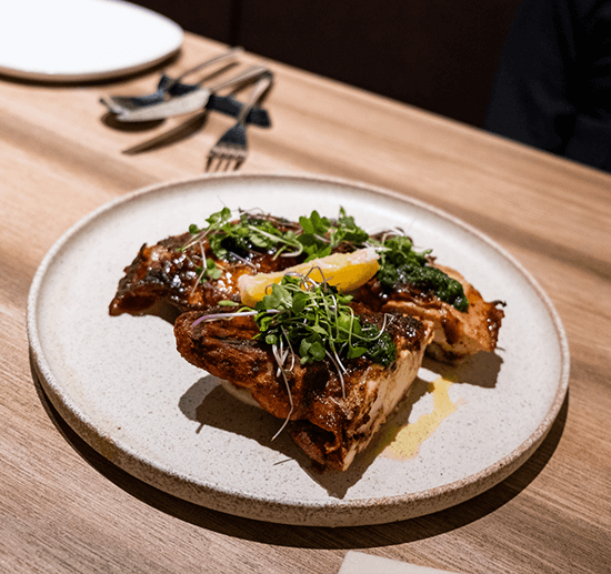 Oven roasted chicken glazed dark and piled with microgreens and a lemon wedge on a speckled plate