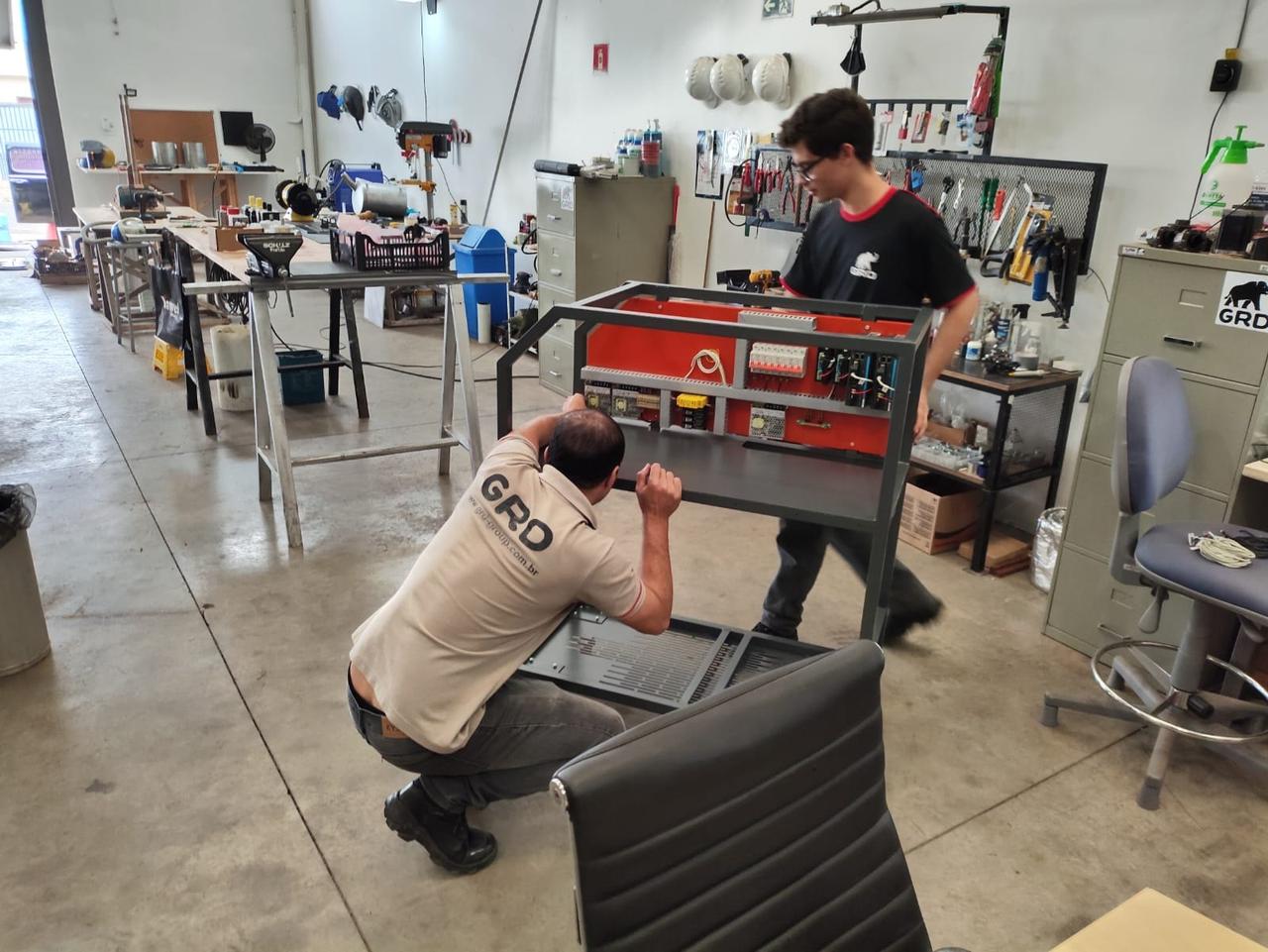 Técnicos da GRD trabalhando no salão do barracão, entre bancadas e máquinas em montagem
