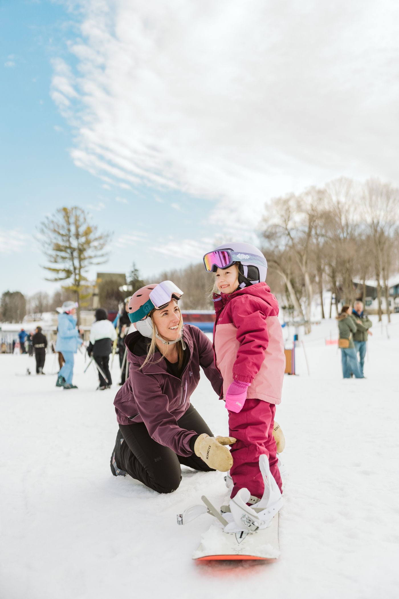 A mom helping a child on a snowboard