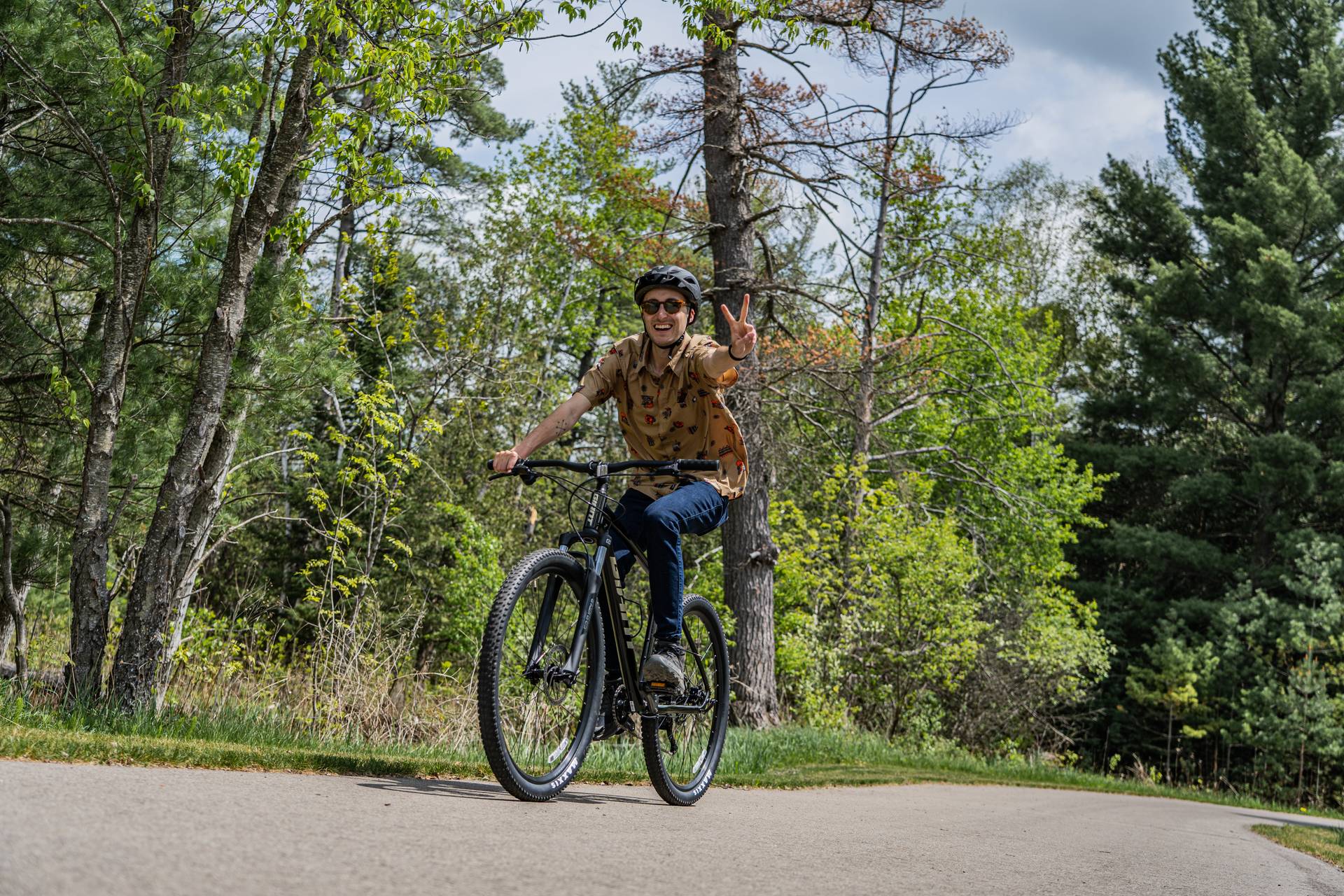 Man riding on bike on the paved trail giving a piece sign.
