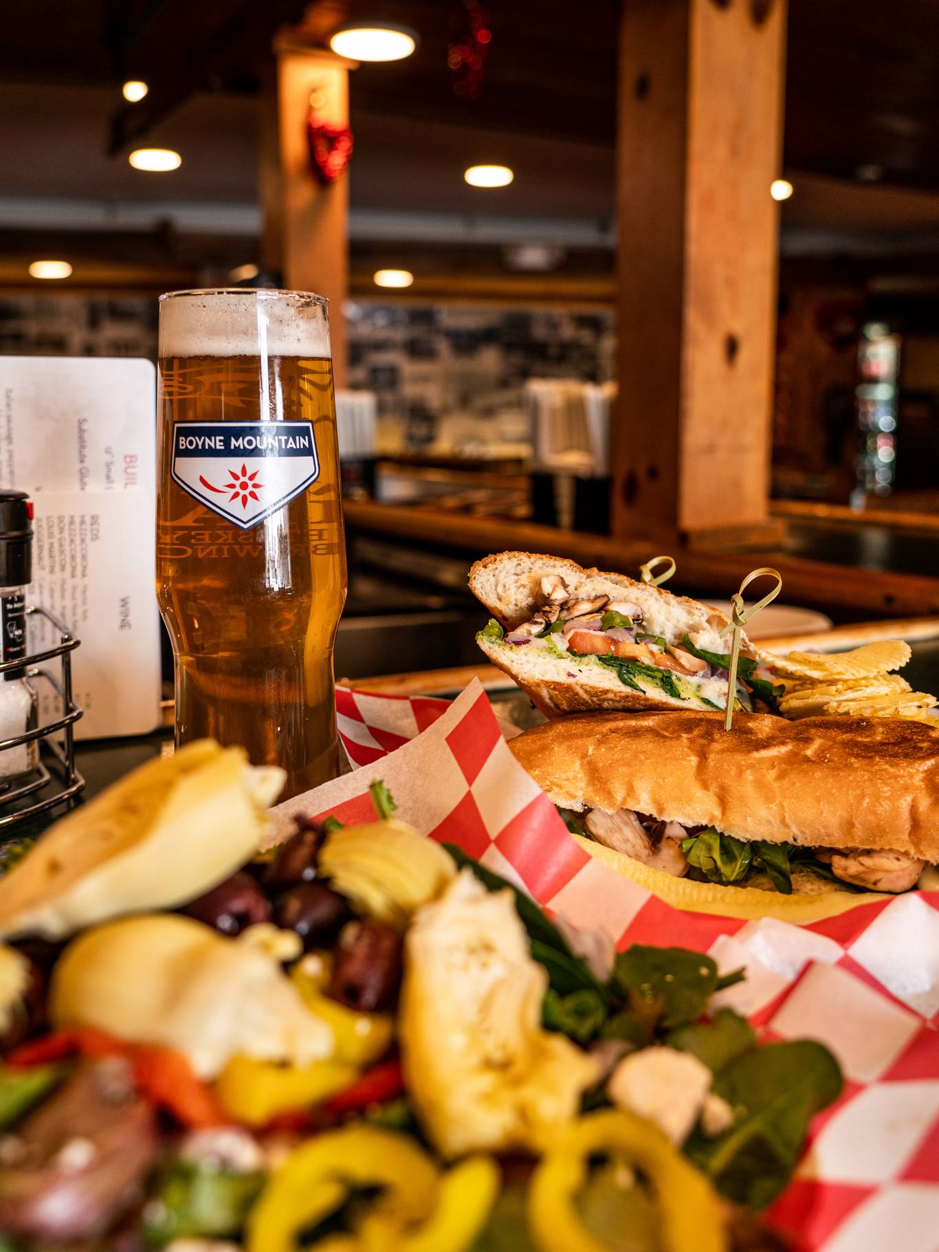 Spread of food showing a salad, grinder, and beer at Trophy Room Pizzeria & Pub at Boyne Mountain