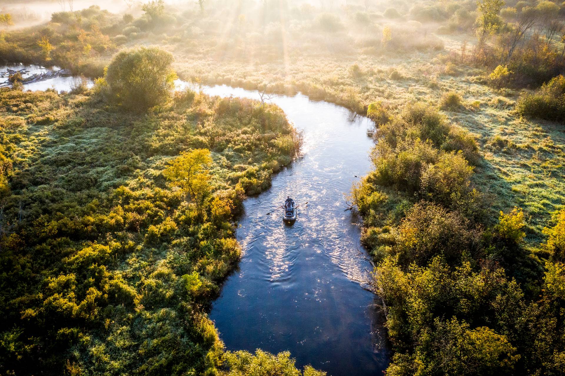 Drone photo of boat floating down the river in morning light.