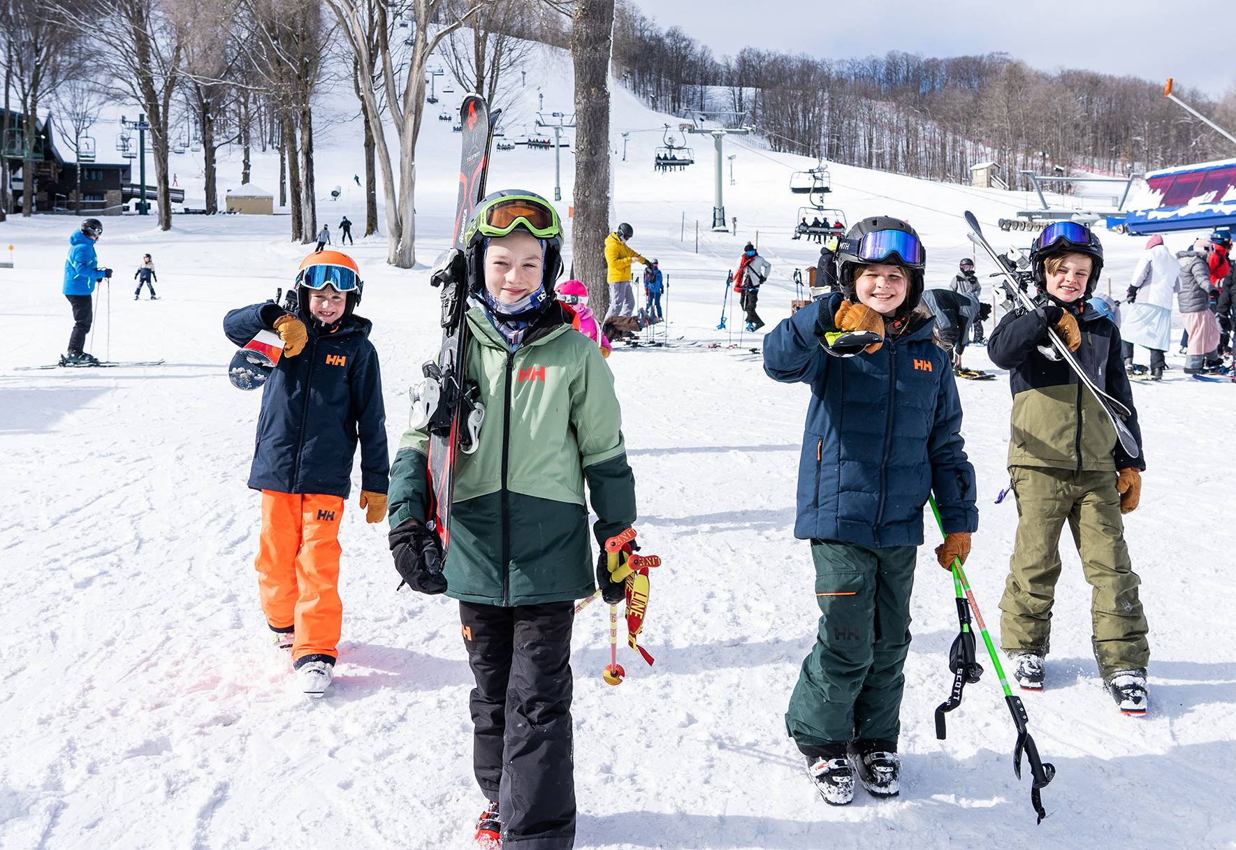 Four kids skier walking at the bottom of the lift with skis on their shoulders.