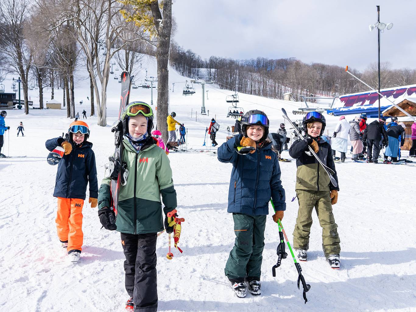 Four kids skier walking at the bottom of the lift with skis on their shoulders.
