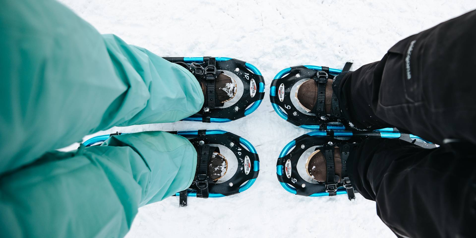 Couple looking down at snowshoes close together.