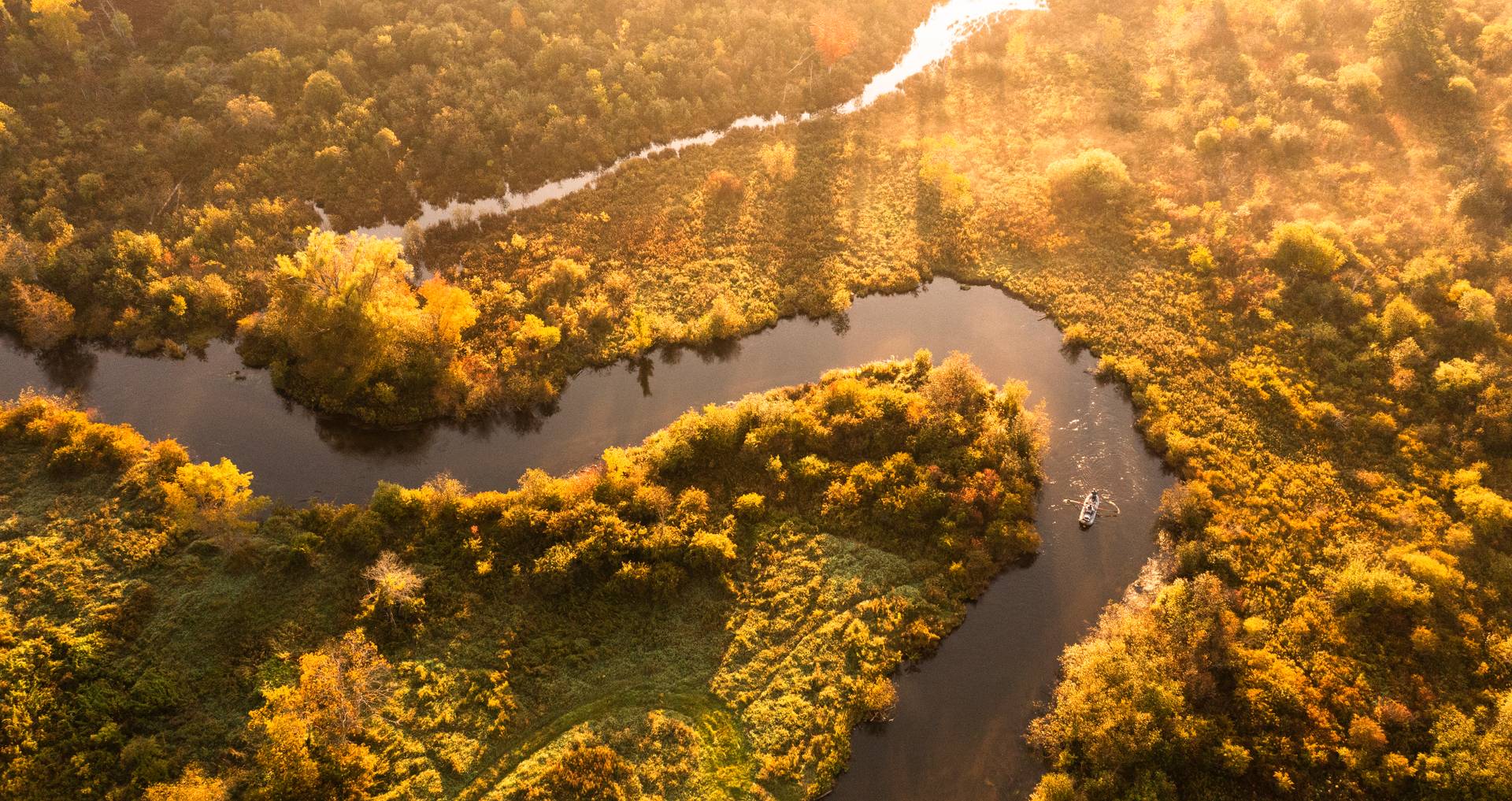 Boat floating down river during golden hour.