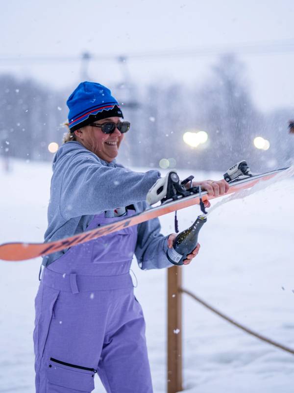 Woman opening a bottle of champagne with a ski