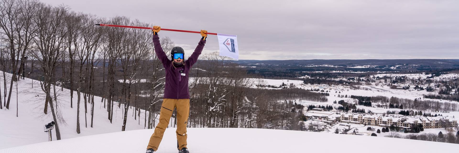 Woman standing at the top of the mountain holding a Boyne Mountain flag