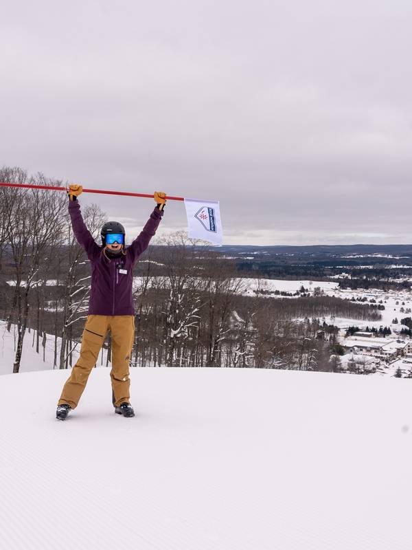 Woman standing at the top of the mountain holding a Boyne Mountain flag